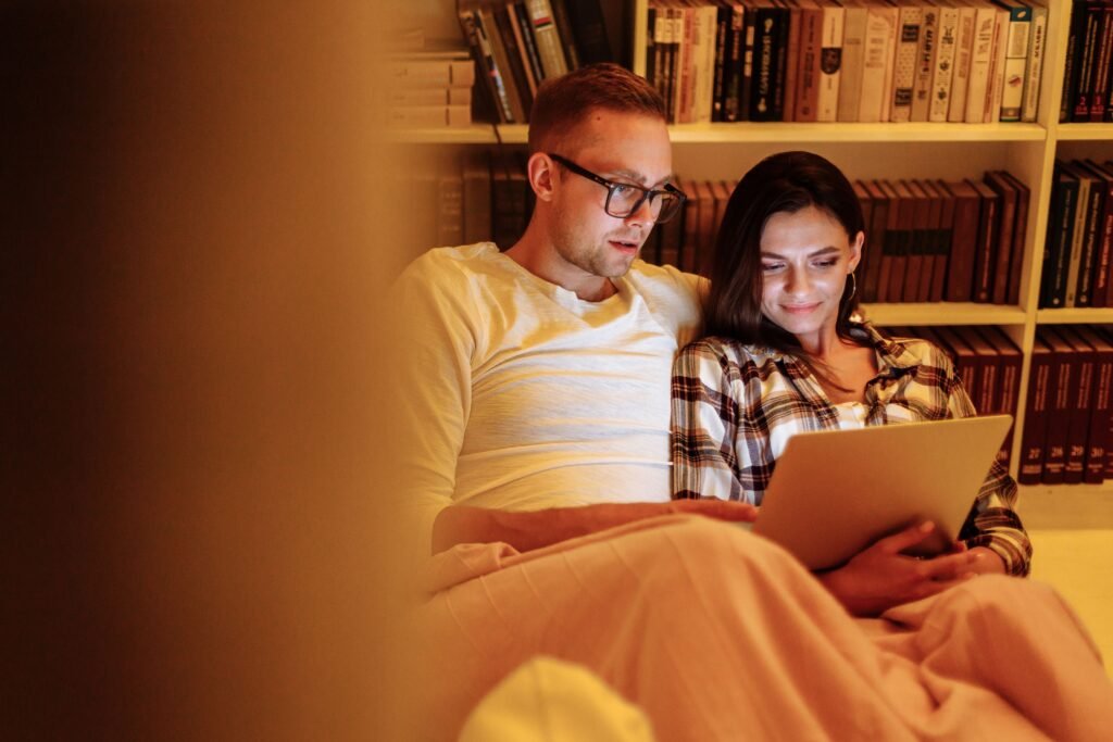 A couple enjoys a cozy evening reading together on a tablet in a home library.
